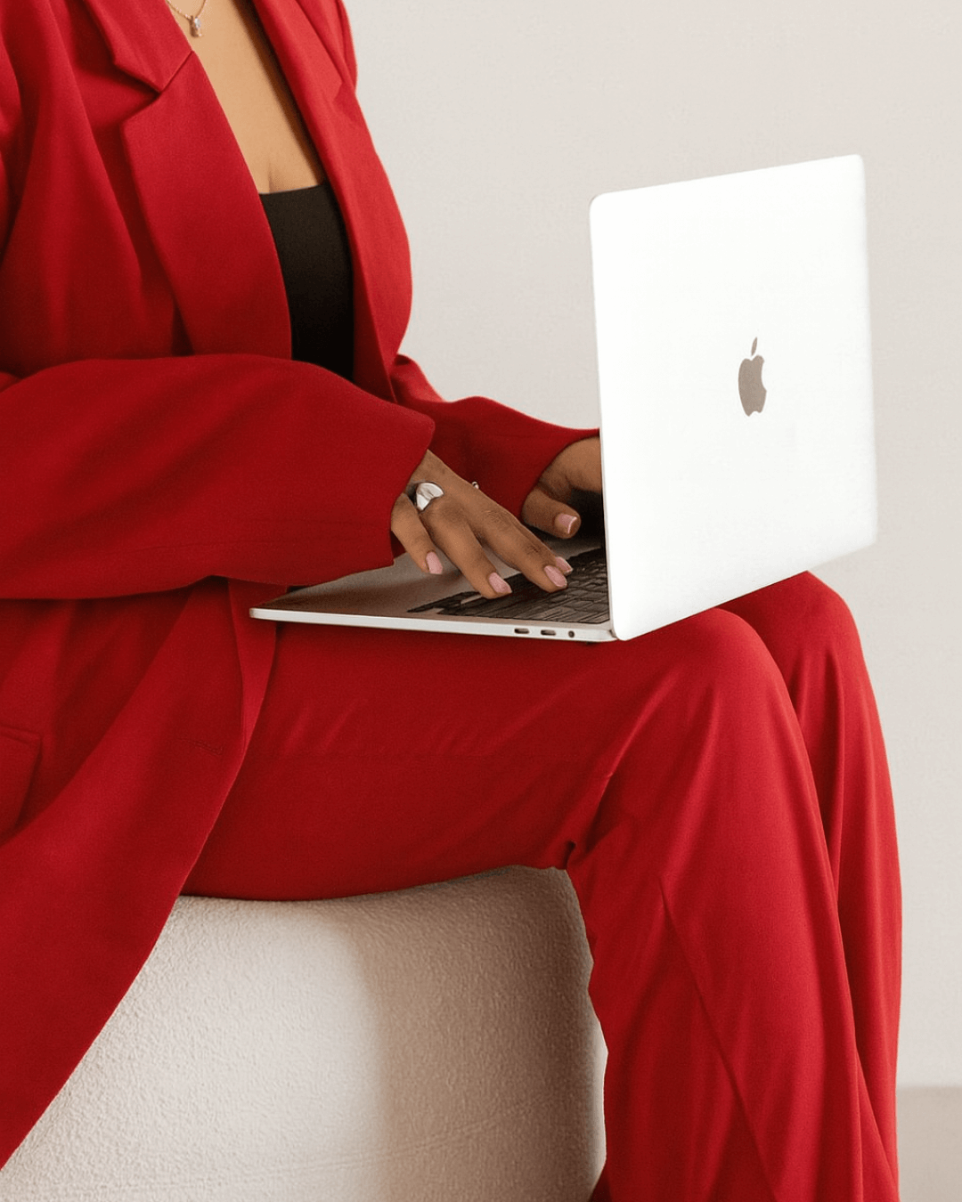 Close-up of a woman in a red suit working on a white Apple MacBook.