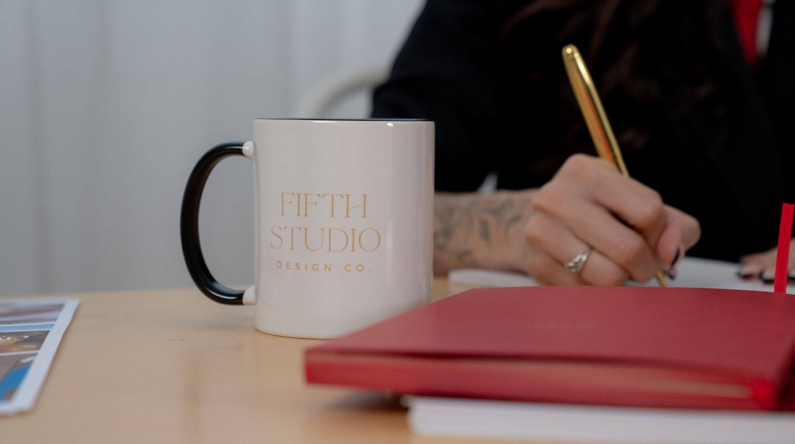 Fifth Studio team member writing notes beside a branded coffee mug and red notebook during a creative strategy session.