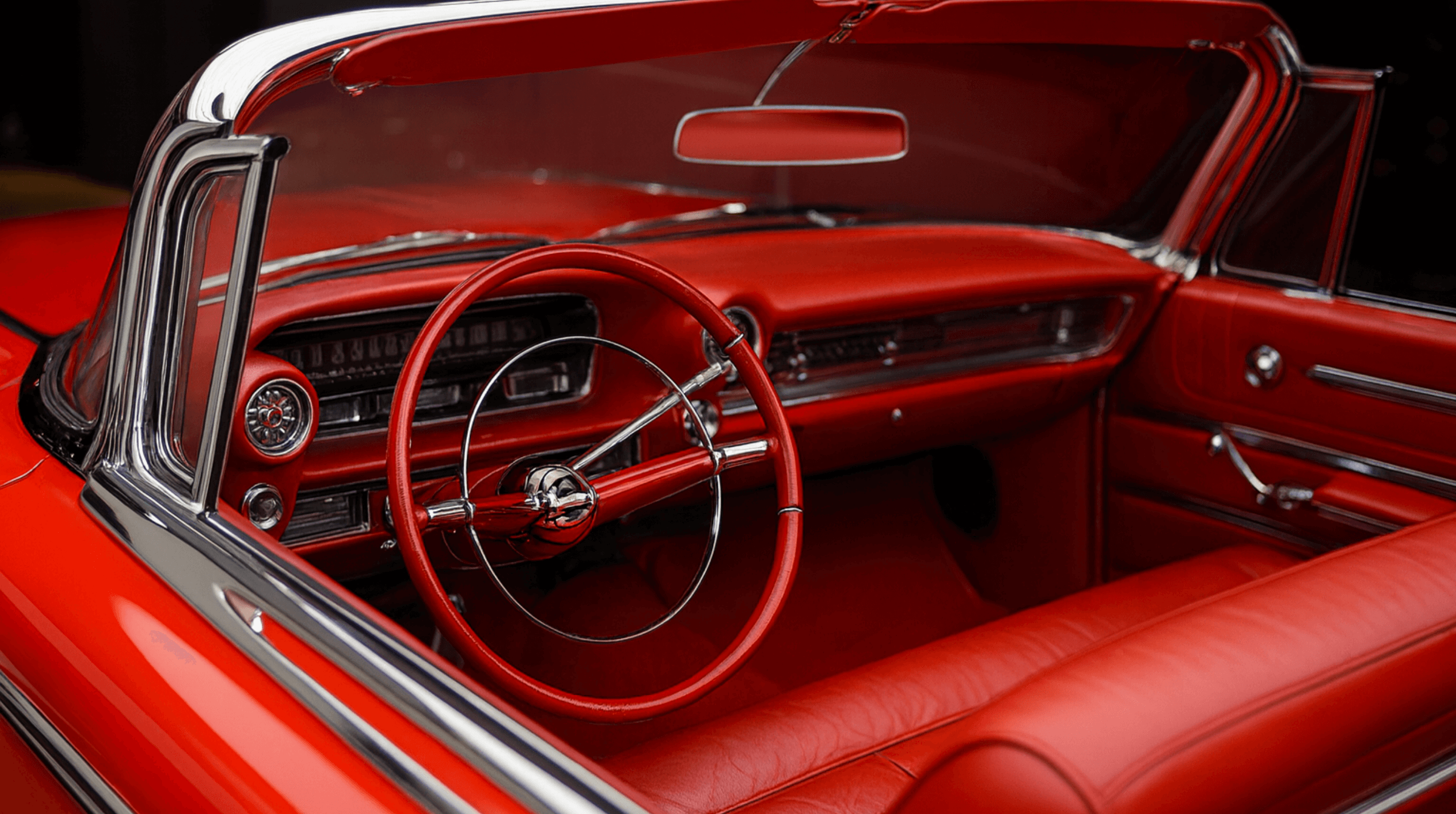 Interior of a classic red convertible car with red leather seats, steering wheel, and dashboard accented with chrome details.