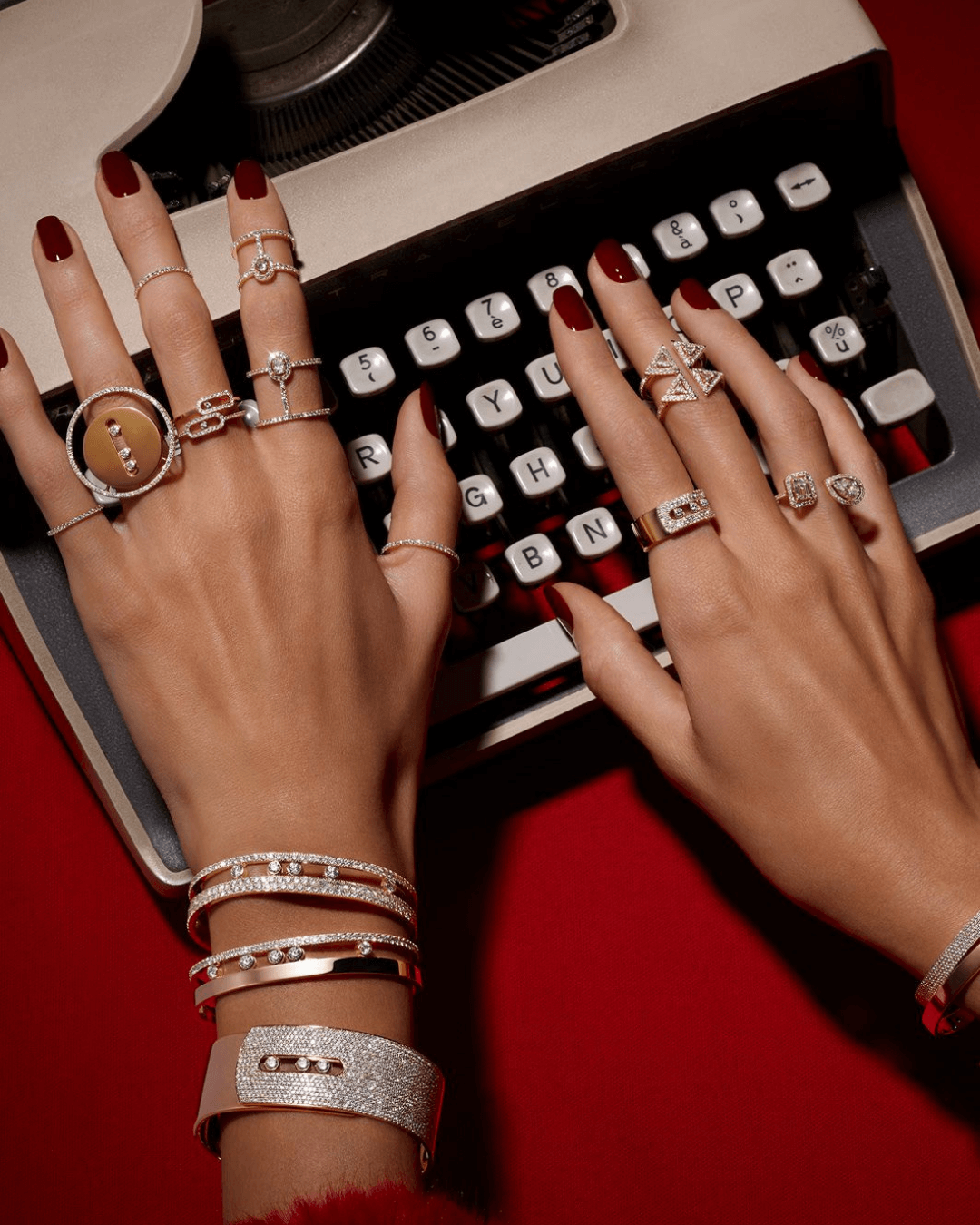 The style is in the details: visual storytelling through type. Hands with statement jewellery typing on a vintage typewriter with bold red background.
