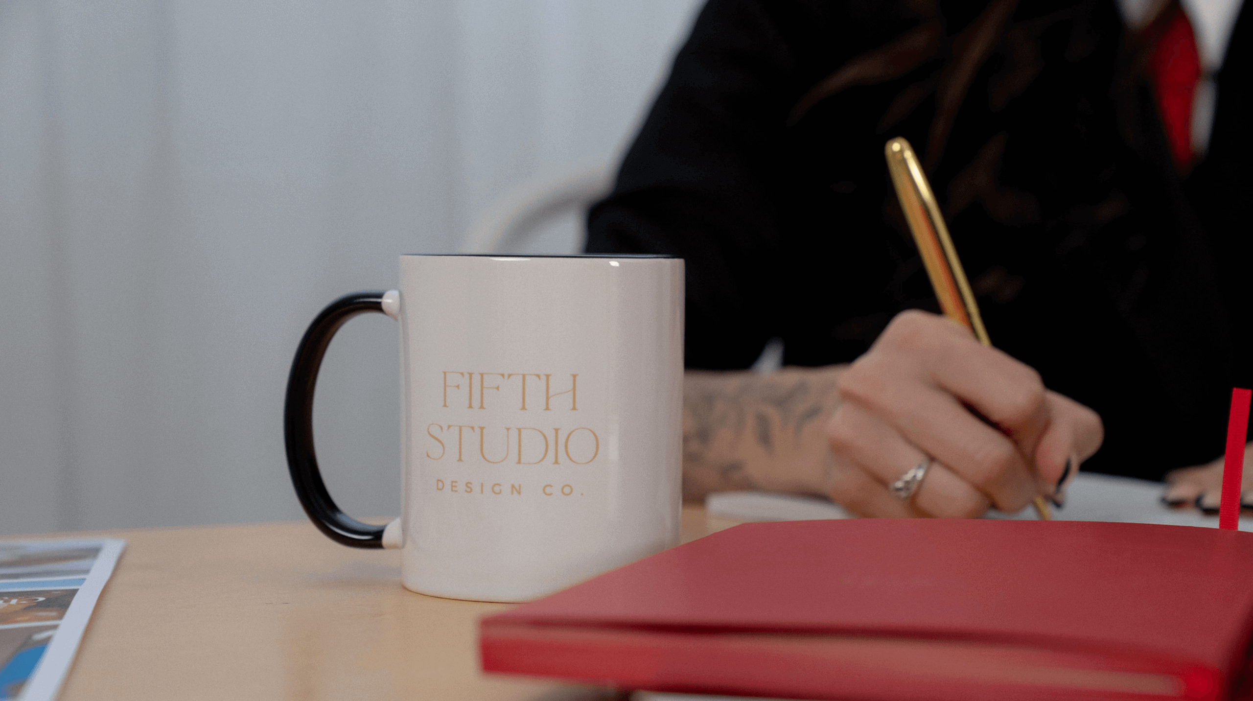 Fifth Studio coffee mug on a desk with red notebook and hand writing in the background