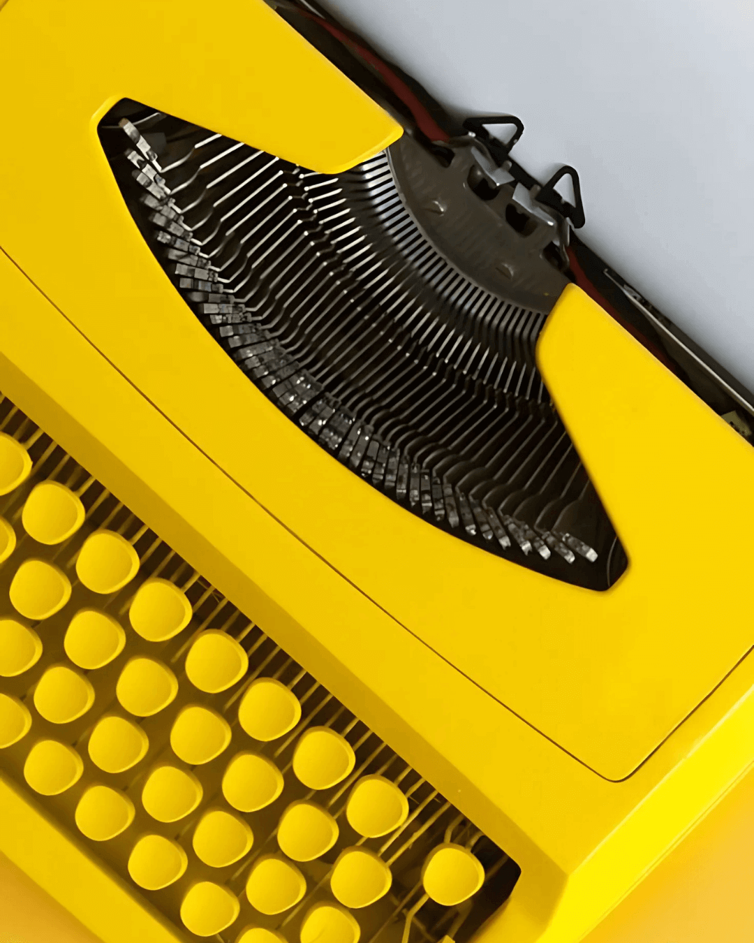 Close-up of a bright yellow typewriter with round keys and metal typebars.