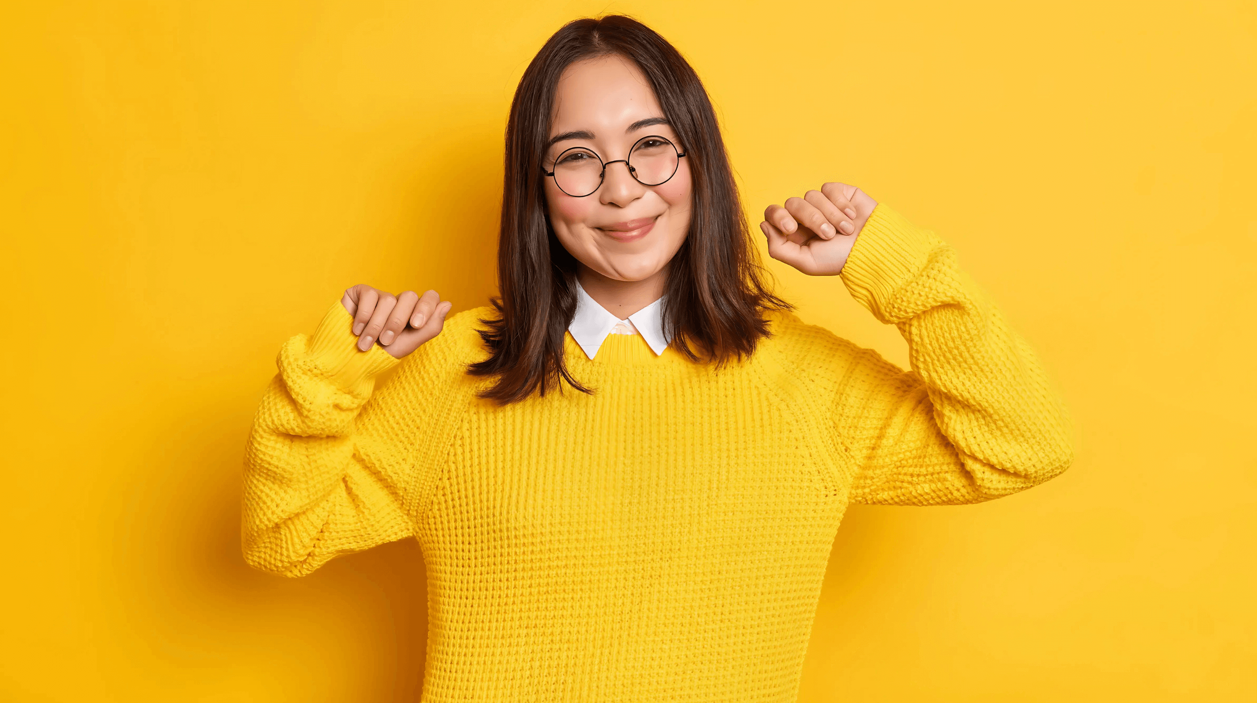 Woman in a yellow sweater smiling against a yellow background.