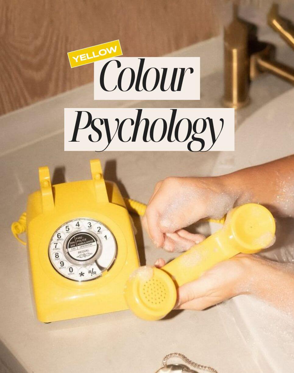 Close-up of a person holding a vintage yellow rotary phone over a bathroom sink filled with bubbles, with text overlay reading “Yellow Colour Psychology.”