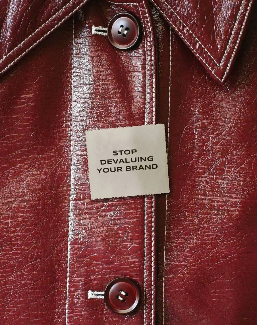 Close-up of a maroon leather jacket with a beige tag that reads “STOP DEVALUING YOUR BRAND.